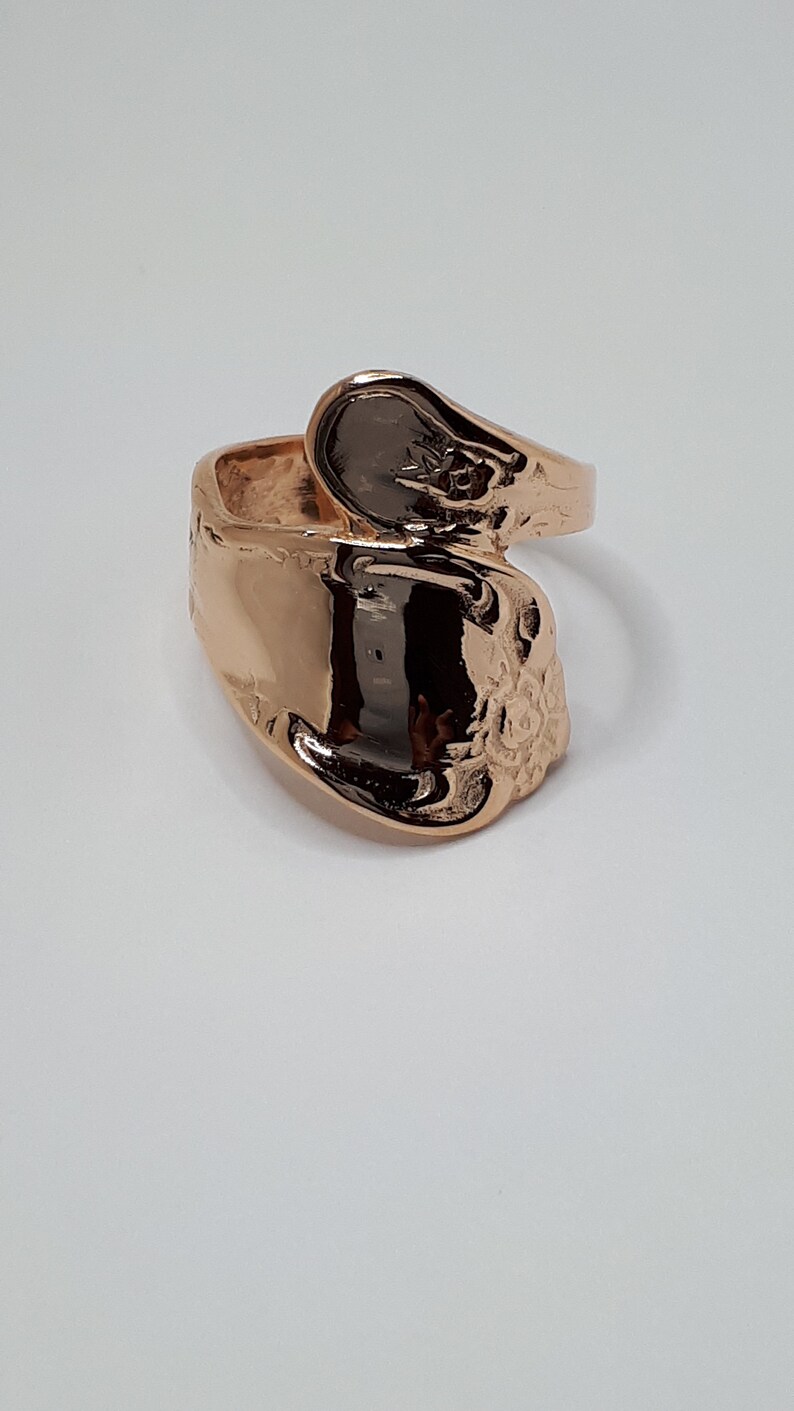 May include: A rose gold spoon ring with a floral design. The ring is made from a repurposed spoon.
