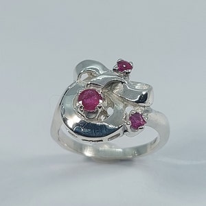 May include: A silver ring with a stylised design featuring three pink ruby gemstones.
