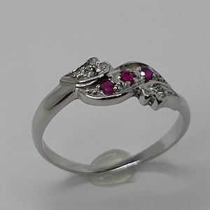 May include: A silver ring with a swirling design set with three red rubies and small diamonds.