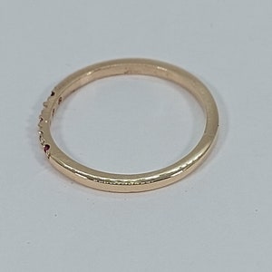 Pode incluir: Um fino anel de banda de ouro com pequenas pedras preciosas vermelhas engastadas na banda.