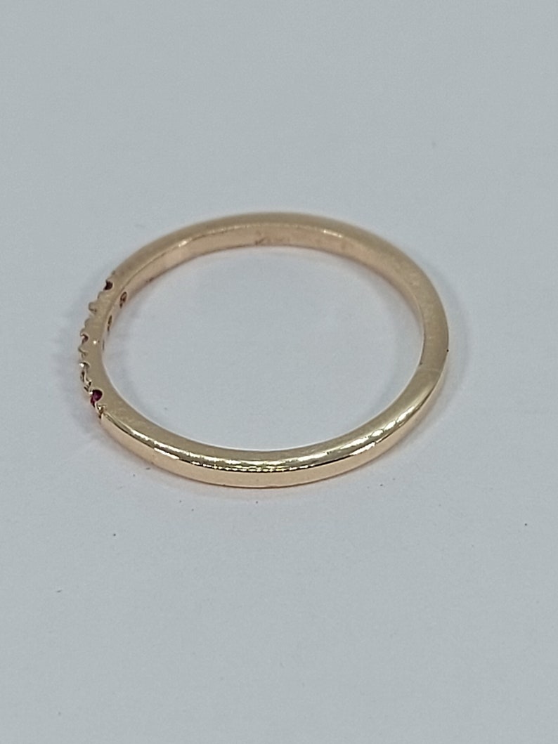 Pode incluir: Um fino anel de banda de ouro com pequenas pedras preciosas vermelhas engastadas na banda.