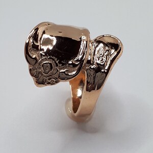 May include: A gold-toned ring with a detailed floral design. The ring is open and designed to fit on the finger.