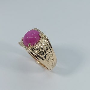 Op de afbeelding: Een gouden ring met een versierd ontwerp en een roze edelsteen.