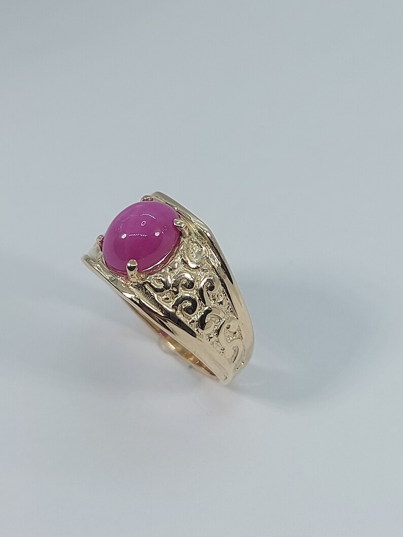 Op de afbeelding: Een gouden ring met een versierd ontwerp en een roze edelsteen.