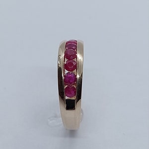 May include: A gold band ring with a row of red rubies set in the centre.