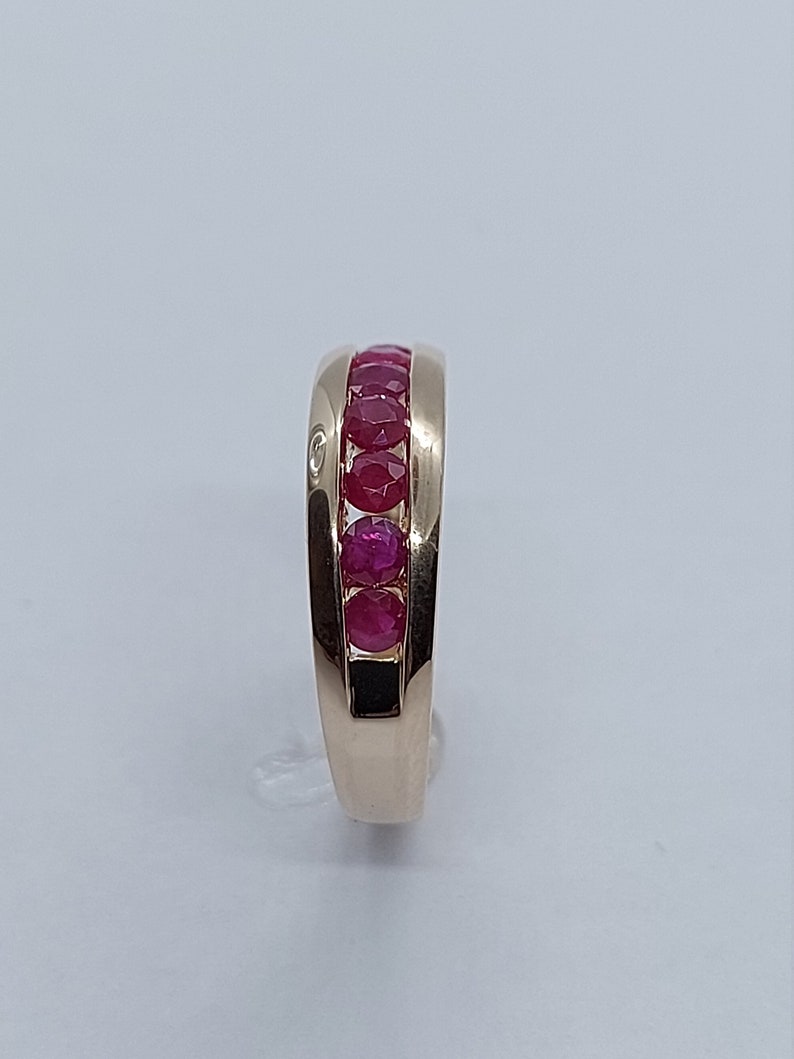 May include: A gold band ring with a row of red rubies set in the centre.