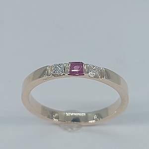 May include: A gold band ring with a single red ruby and two small diamonds.