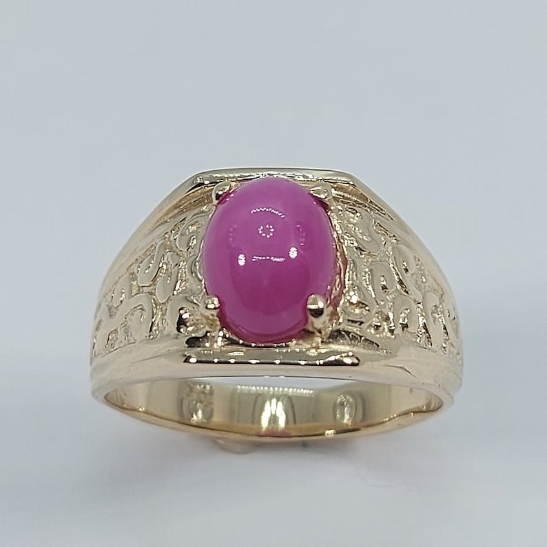 Op de afbeelding: Een gouden ring met een ovale roze edelsteen gezet in een gedetailleerd, versierd ontwerp.