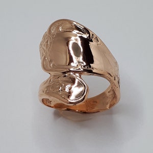 May include: A gold-toned ring made from a bent spoon. The ring is decorated with a floral design and has a shiny finish.