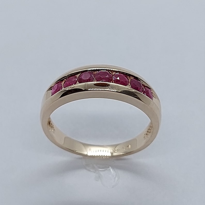 May include: A gold band ring with a row of red ruby stones set in the centre.