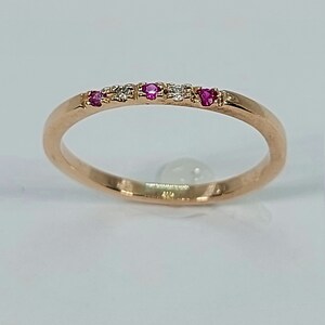 Pode incluir: Um delicado anel de banda de ouro com pedras preciosas rosa e brancas alternadas. O anel &eacute; engastado com pequenas pedras redondas.