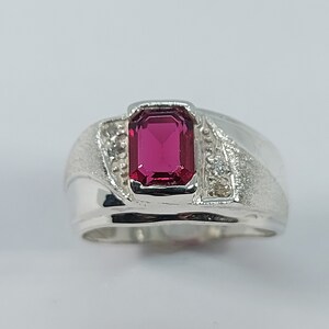 Peut inclure: Une bague en argent avec une pierre précieuse rouge et de petites pierres blanches sur la bande.