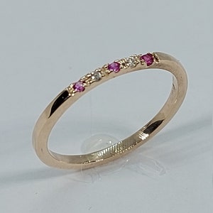Pode incluir: Um delicado anel de banda de ouro com uma fileira de pequenas pedras preciosas rosa e brancas.