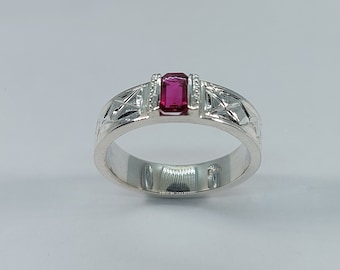 Puede incluir: Un anillo de plata con una piedra preciosa roja engastada en el centro. El anillo tiene un diseño tallado en la banda.