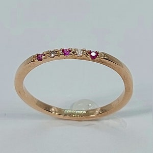 Pode incluir: Um delicado anel de banda de ouro com uma fileira de pequenas pedras preciosas rosa e brancas.