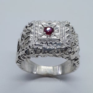 Op de afbeelding: Een zilveren ring met een gedetailleerd ontwerp en een rode edelsteen in het midden.