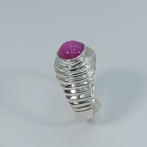 K&ouml;nnte beinhalten: Ein silberner Ring mit einem rosafarbenen Edelstein, der in der Mitte eingesetzt ist. Die Ringschiene ist mit einer Reihe von Rillen strukturiert.