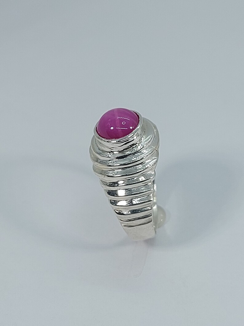 K&ouml;nnte beinhalten: Ein silberner Ring mit einem rosafarbenen Edelstein, der in der Mitte eingesetzt ist. Die Ringschiene ist mit einer Reihe von Rillen strukturiert.