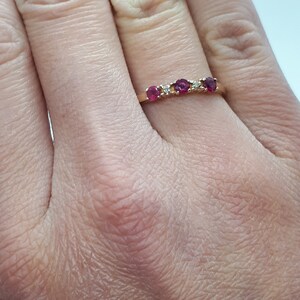 May include: A gold band ring with five red gemstones and two small white gemstones.