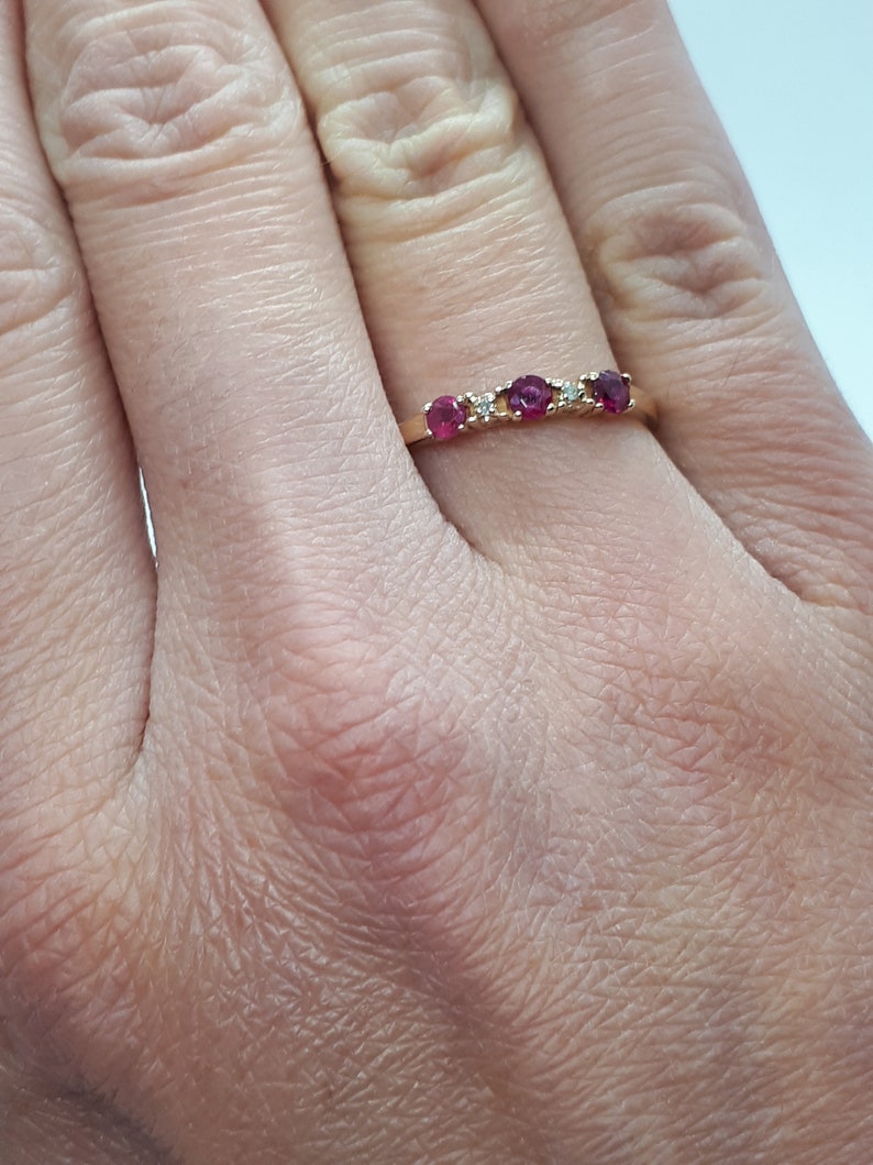 May include: A gold band ring with five red gemstones and two small white gemstones.