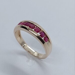 May include: A gold band ring with a row of red ruby stones set in the centre.