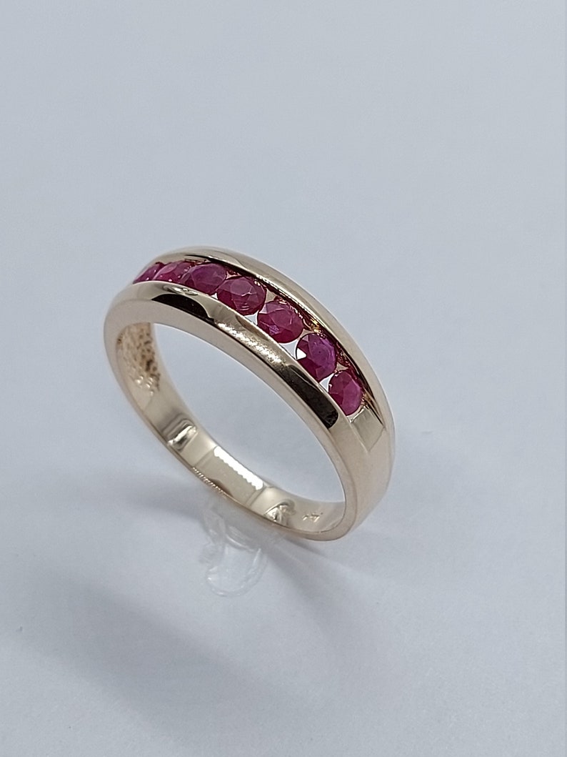 May include: A gold band ring with a row of red ruby stones set in the centre.