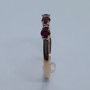 May include: A gold band ring with five red gemstones and small white gemstones set in the band.