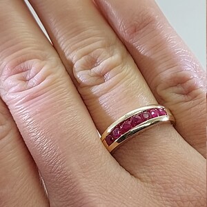 May include: A gold band ring with a row of red ruby stones set in a curved design.