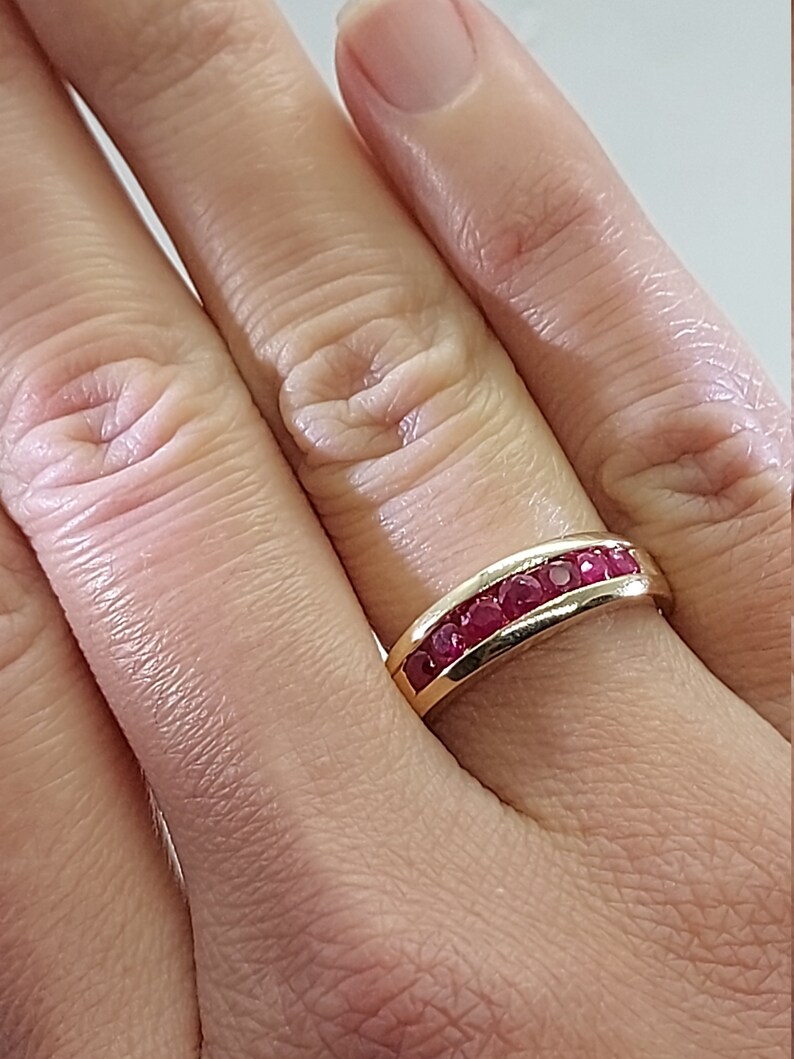 May include: A gold band ring with a row of red ruby stones set in a curved design.