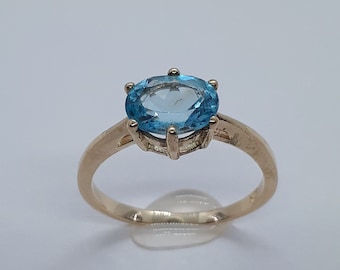 Op de afbeelding: Een gouden ring met een lichtblauwe ovale edelsteen in een kraalbezetting.