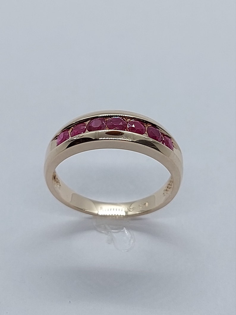May include: A gold band ring with a row of red ruby stones set in the band.