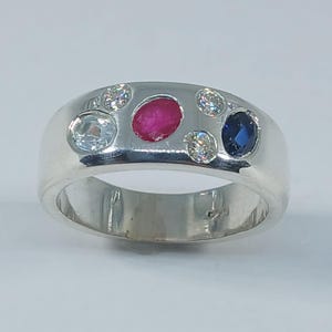 Peut inclure: Une bague en argent avec un rubis rouge, un saphir bleu et plusieurs diamants clairs.