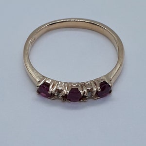May include: A gold band ring with three ruby stones and a small diamond between each ruby.