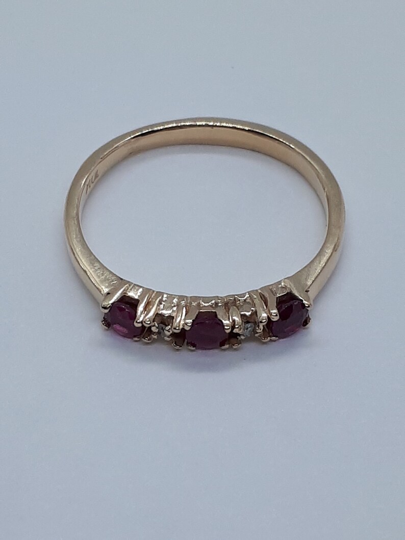 May include: A gold band ring with three ruby stones and a small diamond between each ruby.