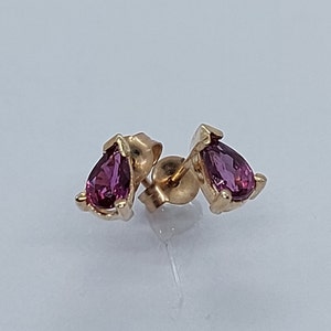May include: A pair of gold earrings with teardrop-shaped pink gemstones.