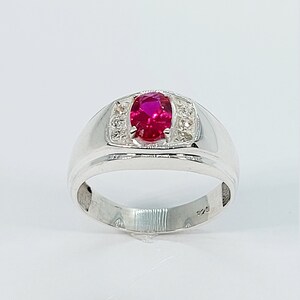May include: A silver ring with a large oval-shaped ruby gemstone surrounded by smaller white gemstones.