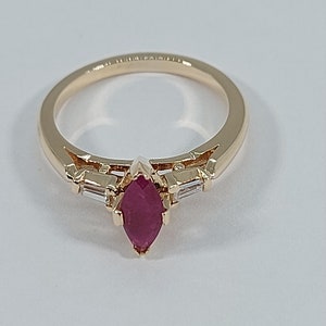 May include: A gold ring featuring a marquise-shaped ruby gemstone, flanked by two smaller baguette-shaped diamonds.