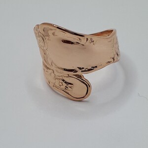 May include: A rose gold spoon ring with a floral design. The ring is made from a vintage spoon and is a unique piece of jewelry.