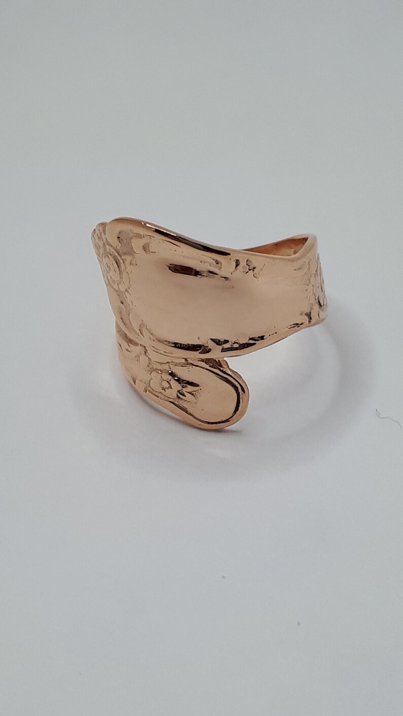 May include: A rose gold spoon ring with a floral design. The ring is made from a vintage spoon and is a unique piece of jewelry.