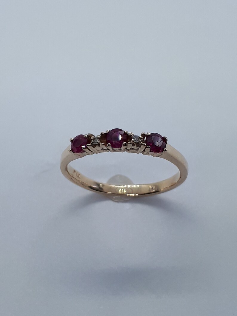 May include: A gold band ring with three red ruby stones and two small diamonds.