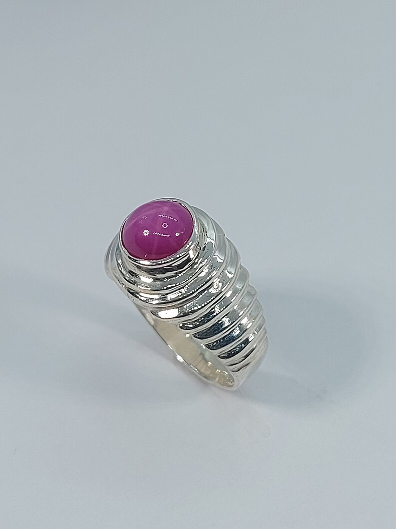 K&ouml;nnte beinhalten: Ein silberner Ring mit einem rosafarbenen Edelstein, der in einem strukturierten Band gefasst ist.