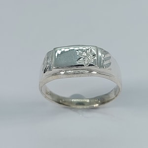 May include: A silver ring with a rectangular band and a floral design on the top.