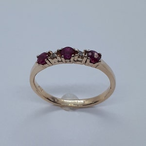 May include: A gold band ring with three red ruby stones and small diamonds set in the band.