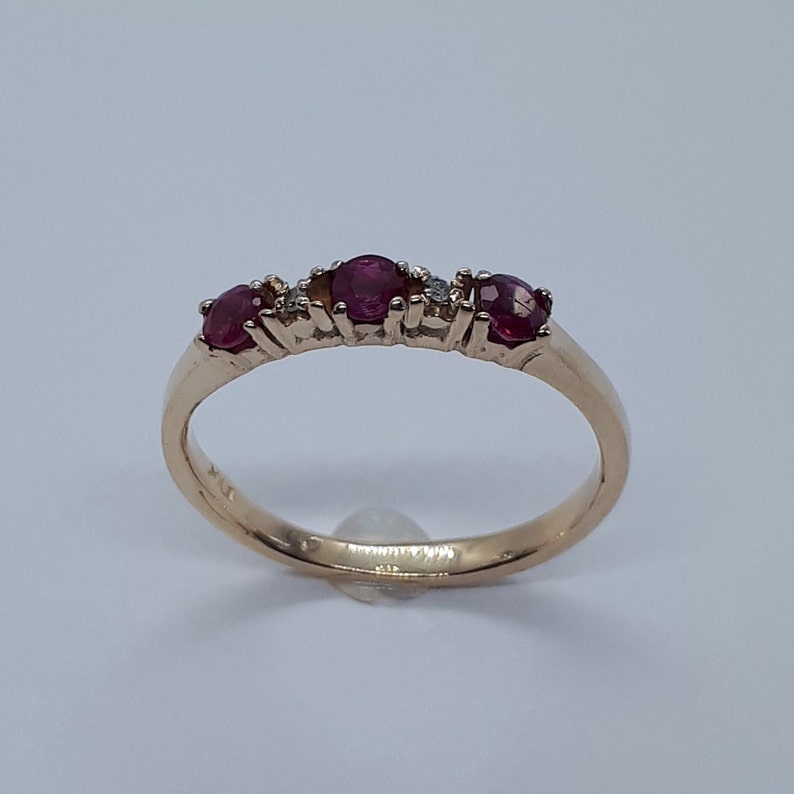 May include: A gold band ring with three red ruby stones and small diamonds set in the band.