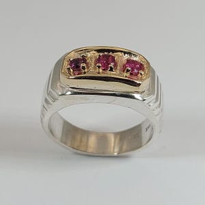 Peut inclure: Une bague bicolore composée d'un large anneau en argent aux côtés texturés et d'une plaque supérieure rectangulaire en or. La plaque en or est sertie de trois pierres précieuses rondes, facettées et rose foncé, disposées horizontalement.