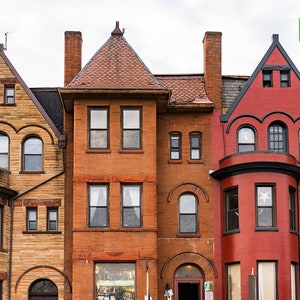 Peut inclure: Une rangée de cinq maisons en briques avec des styles architecturaux différents. Les maisons sont peintes dans des tons de rouge, de brun et de beige. Les maisons ont plusieurs fenêtres et portes.