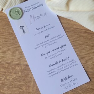 Peut inclure: Menu de mariage imprimé sur papier blanc avec un sceau de cire vert et le nom "Izaac". Le menu comprend du texte français avec des plats comme de l'agneau et des desserts. La date est le 13 août 2025.