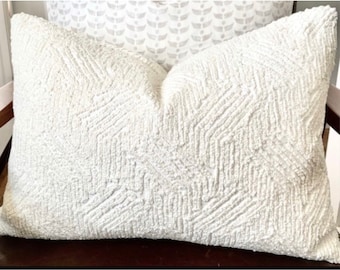 May include: A rectangular throw cushion in a solid off-white colour featuring a raised, textured chevron pattern across the entire front surface. The fabric has a nubby, tactile quality that creates a distinct geometric design through depth and shadow.