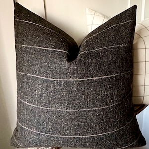 May include: A dark gray throw pillow with white stripes. The pillow is made of a textured fabric and has a square shape.