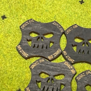 May include: Five wooden skull-shaped tokens with the words "No Zone" and "No On" around the edges. The tokens are black with gold lettering.